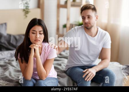 Marito che tocca offeso moglie spalla seduto a letto a casa Foto Stock