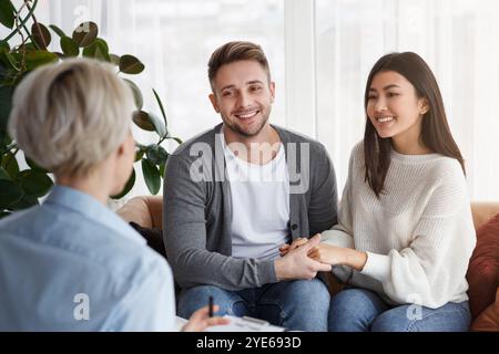 Sorridenti coniugi multietnici mani che riconciliano i loro collaboratori seduti nell'Ufficio Psicoterapeuta Foto Stock