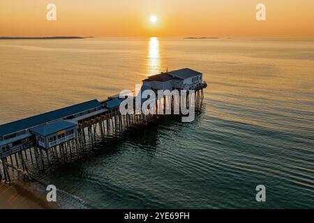 Il molo di Old Orchard Beach si estende in acque calme sotto una calda alba, con edifici sopraelevati sopra il mare su palafitte. La luce del sole si riflette sulla o Foto Stock