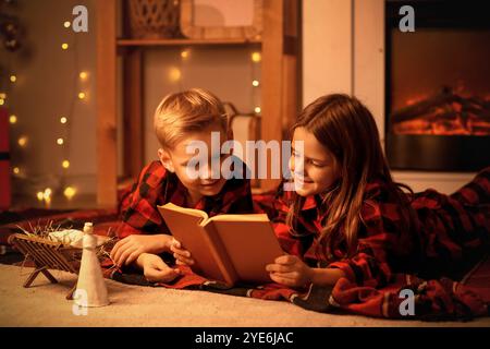 Bambini piccoli che leggono la storia di Natale su plaid a casa la sera Foto Stock