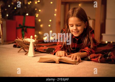 Bambina che legge la storia di Natale su plaid a casa la sera Foto Stock