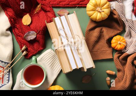 Composizione con libri, tazza di tè, abiti caldi e zucche su sfondo verde Foto Stock