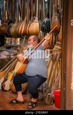 Kashgar, Cina - 17 LUGLIO 2022: Uomo uiguro seduto e suonando strumenti uiguri tradizionali nel suo negozio di strumenti musicali in un mercato locale nella vecchia Ka Foto Stock