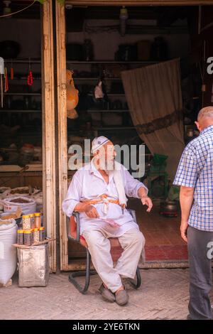 Kashgar, Cina - 17 LUGLIO 2022: Uomo uiguro seduto nel suo negozio di spezie in un mercato locale nel vecchio Kashgar Foto Stock