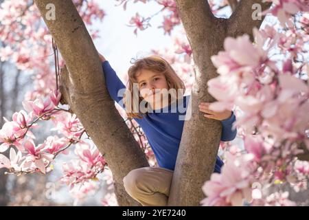 Divertimento primaverile per i bambini. I bambini giocano all'aperto in uno splendido giardino primaverile. Faccia di ragazzo in fiori. Adorabile ragazzino nel giardino dei ciliegi in fiore su un bellissimo giardino Foto Stock