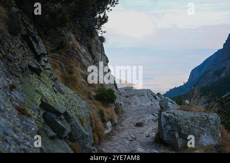 Sentiero roccioso con catene che conducono lungo la montagna, che offre una vista panoramica della valle durante il tramonto. Foto Stock