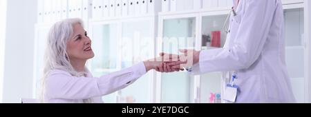 Il medico biondo positivo saluta con la donna matura di handshake Foto Stock