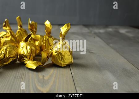 Caramelle al cioccolato in involucri dorati gialli su sfondo grigio con spazio per testo copyspace. Caramelle come regalo. Giornata del cioccolato. Foto Stock