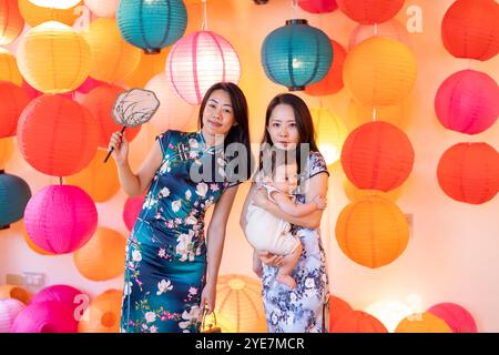 Due donne di 30 anni che indossano abiti tradizionali cinesi tengono un bambino di 6 mesi in un colorato posto adatto alle foto a Taipei, Taiwan, a settembre. Foto Stock