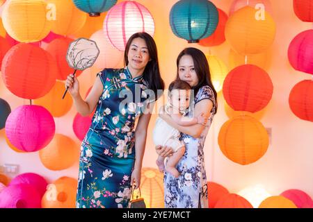 Due donne di 30 anni che indossano abiti tradizionali cinesi tengono un bambino di 6 mesi in un colorato posto adatto alle foto a Taipei, Taiwan, a settembre. Foto Stock