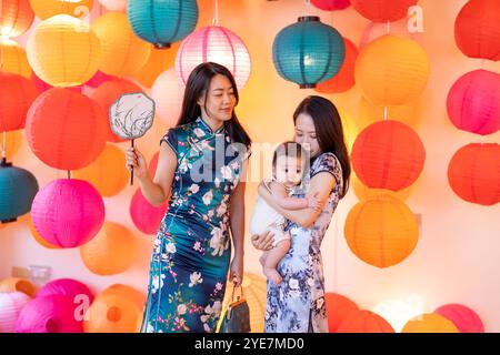 Due donne di 30 anni che indossano abiti tradizionali cinesi tengono un bambino di 6 mesi in un colorato posto adatto alle foto a Taipei, Taiwan, a settembre. Foto Stock