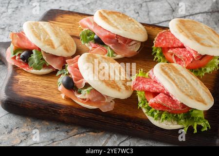 Piccoli panini con tigelle italiane con salsiccia, jamon e verdure fresche da vicino su tavola di legno. Orizzontale Foto Stock