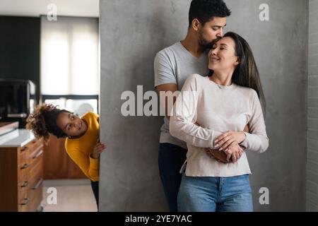 La bella coppia multietnica passa del tempo insieme, abbracciando e sorridendo con il bambino sullo sfondo Foto Stock