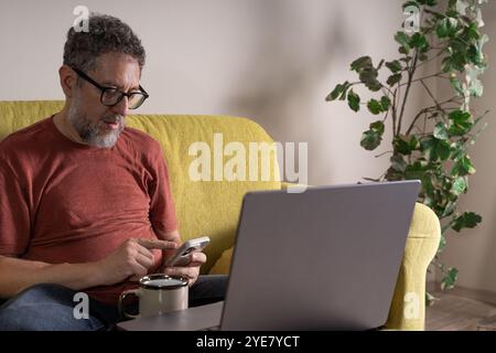 Uomo maturo contemporaneo che gestisce dispositivi digitali in casa. Ritratto naturale di uno stile di vita professionale di mezza età che lavora in remoto con Foto Stock