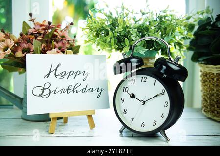 Happy Birthday cita il testo su carta con cavalletto e sveglia sullo sfondo della finestra Foto Stock