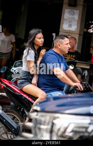 Un uomo occidentale si fa strada lungo Soi Buakhao, Pattaya, Thailandia, con una giovane signora thailandese sul retro dello scooter o della bici. Foto Stock