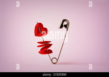 Spilla di sicurezza con cuori su sfondo rosa - concetto di amore Foto Stock