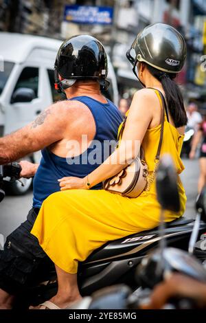 Un uomo occidentale si fa strada lungo Soi Buakhao, Pattaya, Thailandia, con una giovane signora thailandese sul retro dello scooter o della bici. Foto Stock