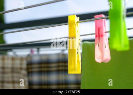 Asciugare la biancheria in una giornata di sole: Un primo piano di clothespins di plastica colorata appesi su aste di una griglia di asciugatura esterna sullo sfondo di vestiti Foto Stock