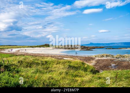 Camminatore e paddleboarder sulla spiaggia di Traigh vicino a Portnaluchaig a Lochaber, Highlands scozzesi, Scozia, con l'isola di Eigg in lontananza Foto Stock