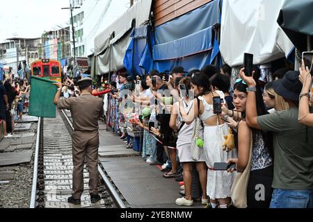 Mercato ferroviario Tailandia, stazione principale segnala il treno sventolando bandiere rosse e verdi, sgombrando i binari, i turisti stanno scattando con ansia foto in cellulare Foto Stock