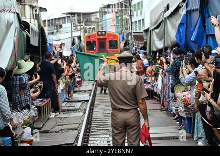 Mercato ferroviario Tailandia, stazione principale segnala il treno sventolando bandiere rosse e verdi, sgombrando i binari, i turisti stanno scattando con ansia foto in cellulare Foto Stock