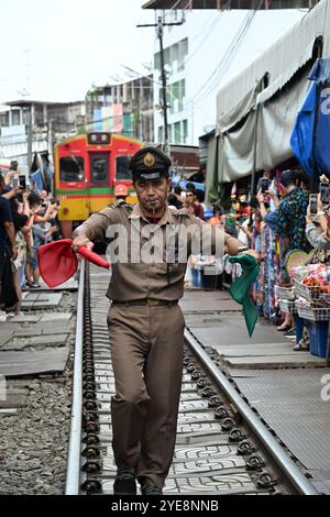 Mercato ferroviario Tailandia, stazione principale segnala il treno sventolando bandiere rosse e verdi, sgombrando i binari, i turisti stanno scattando con ansia foto in cellulare Foto Stock