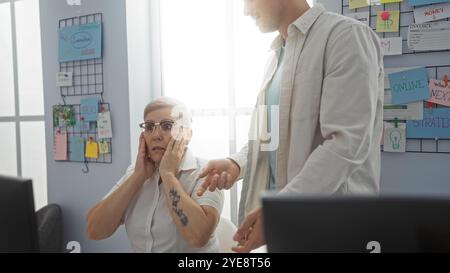 Donna che sembra sorpresa mentre parla con un uomo in ufficio con idee di brainstorming sulla parete in background che mettono in evidenza i lavoratori e la partnership commerciale Foto Stock