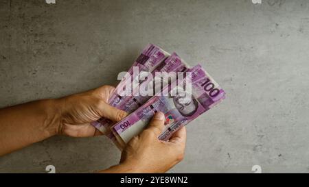 Uomo che tiene in mano più banconote del peso filippino in un contesto concreto, mostrando la valuta filippina in una visione dettagliata delle mani e del denaro. Foto Stock