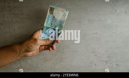 Mano che tiene i dollari di hong kong su sfondo di cemento con dita visibili che afferrano le banconote, mostrando caratteristiche distintive della valuta. Foto Stock