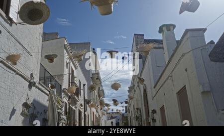 Affascinante strada di alberobello, in italia, decorata con cappelli appesi in una giornata di sole, che mostra gli unici edifici in pietra bianca della città e la vibrante atmos Foto Stock