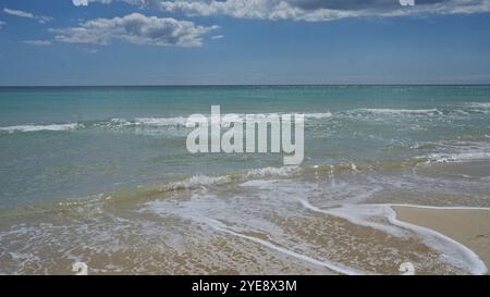 Una giornata serena alla spiaggia di pescoluse nel salento, puglia, italia, caratterizzata da acque turchesi cristalline, onde dolci, spiaggia sabbiosa e un cielo blu con Foto Stock