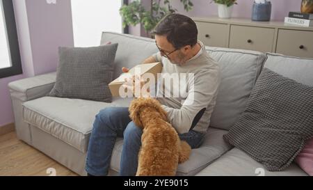 Un uomo di mezza età e un barboncino che interagiscono su un divano all'interno di un accogliente soggiorno, raffigurando compagnia e vita domestica. Foto Stock