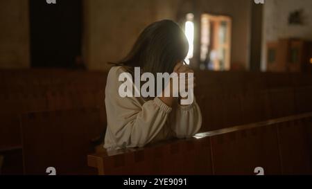 Una bella giovane donna ispanica è vista pregare in una chiesa tranquilla in italia, creando un ambiente cristiano sereno e riverente. Foto Stock