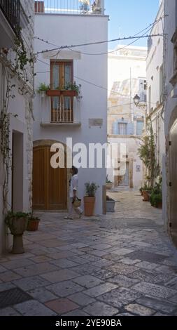 Giovane donna ispanica passeggiando per le affascinanti strade di polignano a mare in puglia, italia, europa, circondata da edifici rustici e sentieri in pietra. Foto Stock