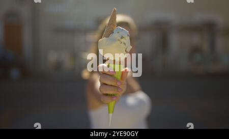 Una giovane donna regala un cono di gelato che si scioglie in una giornata di sole per le strade di gallipoli, puglia, italia, catturando l'essenza dell'estate con un effetto sfocato Foto Stock