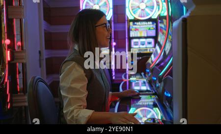 Donna che si diverte a giocare d'azzardo in un vivace casinò di Las vegas, sorridendo accanto alle slot machine incandescenti all'interno. Foto Stock