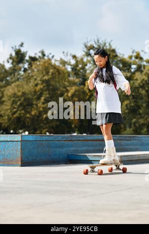 Una giovane ragazza asiatica mostra le sue abilità di pattinaggio indossando un abbigliamento alla moda in un ambiente all'aperto vivace. Foto Stock