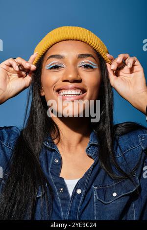 Una giovane donna allegra sfoggia la sua moda autunnale con un cappello giallo su uno sfondo blu. Foto Stock