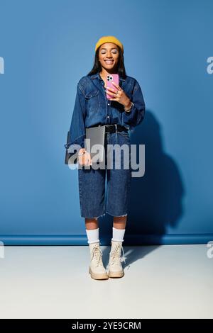 Una giovane donna con un sorriso caldo mostra il suo outfit autunnale alla moda mentre tiene in mano un telefono. Foto Stock