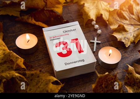 Baviera, Germania - 30 ottobre 2024: Calendario con data ottobre 31. Festa del giorno della riforma e Halloween in un giorno, circondato da foglie autunnali e lume di candela *** Kalender mit Datum 31 Oktober. Reformationstag Feiertag und Halloween an einem Tag, umgeben von Herbstblättern und Kerzenlicht Foto Stock