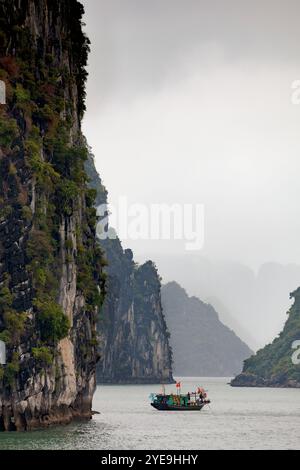 Barca solitaria tra le formazioni rocciose carsiche nella baia di ha Long in Vietnam; Vietnam Foto Stock