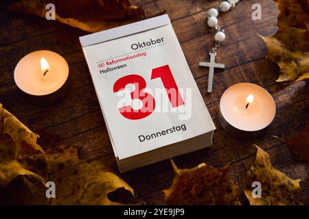 Baviera, Germania - 30 ottobre 2024: Calendario con data ottobre 31. Festa del giorno della riforma e Halloween in un giorno, circondato da foglie autunnali e lume di candela *** Kalender mit Datum 31 Oktober. Reformationstag Feiertag und Halloween an einem Tag, umgeben von Herbstblättern und Kerzenlicht Foto Stock