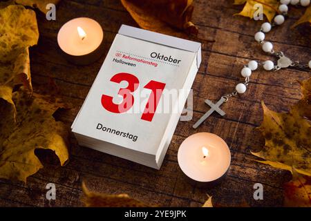 Baviera, Germania - 30 ottobre 2024: Calendario con data ottobre 31. Festa del giorno della riforma e Halloween in un giorno, circondato da foglie autunnali e lume di candela *** Kalender mit Datum 31 Oktober. Reformationstag Feiertag und Halloween an einem Tag, umgeben von Herbstblättern und Kerzenlicht Foto Stock