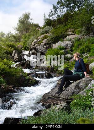 Donna che si gode un momento di tranquillità mentre guarda le gorgoglianti cascate Silverfallet, camminatrice seduto da sola su una roccia nella bellezza naturale della Svezia Foto Stock