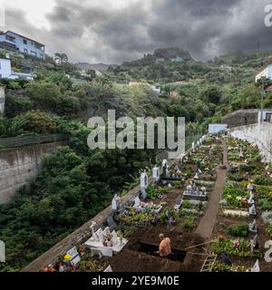 Il giardiniere prepara una sepoltura in un cimitero sotto un cielo pieno di nuvole di tempesta a Porto da Cruz, sull'isola di Madeira, in Portogallo Foto Stock