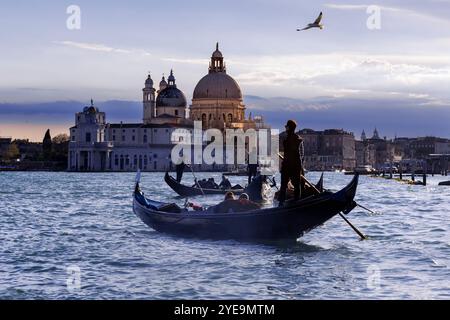Turisti in gondole su un canale al crepuscolo di Venezia. Chiesa di Santa Maria della salute sullo sfondo; Venezia, regione Veneto, Italia Foto Stock