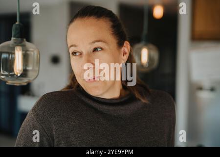 Donna matura sorridente in casuali che guarda lontano da casa Foto Stock