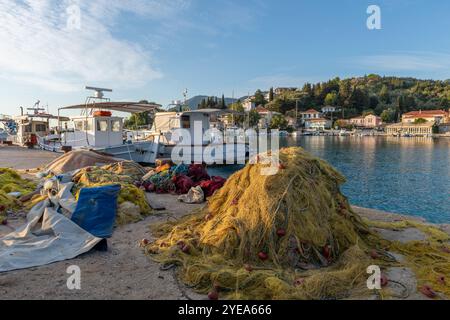 Asciugatura delle reti da pesca sul molo del porto con una barca da pesca tradizionale e vista sull'edificio sul lungomare del villaggio di Lygia, l'isola di Lefkada, Grecia. Foto Stock