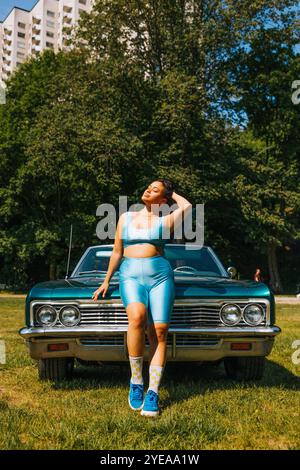 Giovane donna voluttuosa con la mano sui capelli in piedi di fronte all'auto durante il giorno di sole Foto Stock